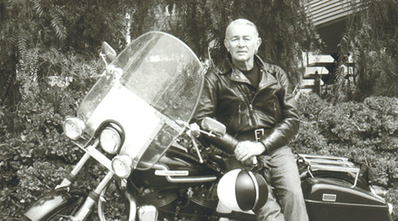 Black and white photo of Roger Hull posing for a photo while sitting on his street motorcycle